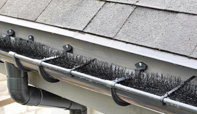 Bottle brush gutter guard installed inside a rain gutter, blocking leaves and debris while allowing water to flow freely through the system