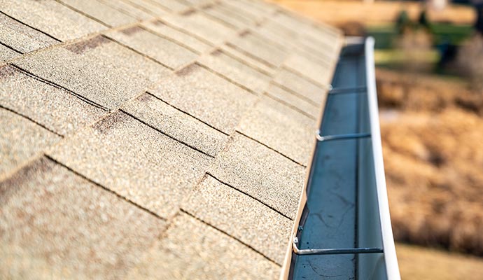 Clean roof gutter along a shingle roof edge showing clear water flow and properly maintained drainage system