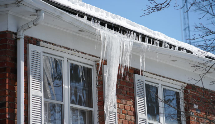 Icicles hanging from a frozen roof gutter on a brick house in winter