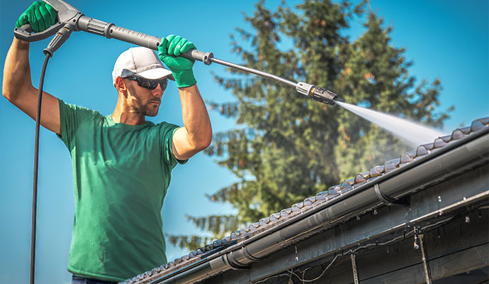 An expert cleaning a gutter with a high-pressure water sprayer