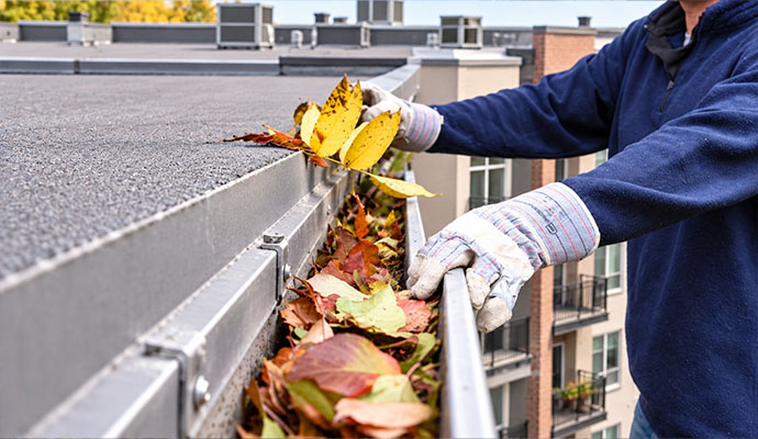 A professional cleaning leaves from gutter system of an apartment building