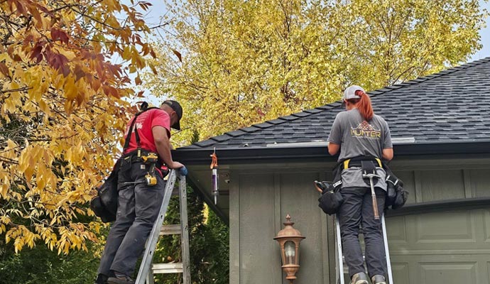 Two professionals repairing gutters on a residential roof to restore proper drainage and prevent water damage.