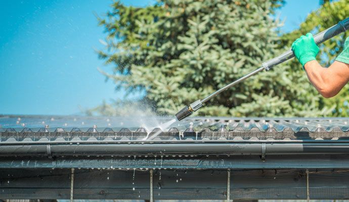 Person cleaning residential gutter using pressure washing equipment
