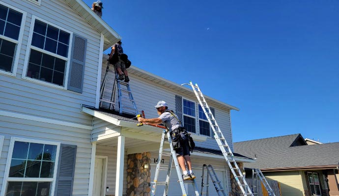 Professionals installing new gutters on a residential home using ladders to ensure proper water drainage and protection.