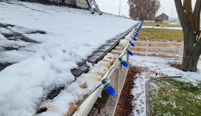 Snow-covered roof and clogged gutter with leaves.