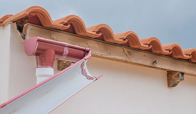 Damaged and detached gutter sagging away from the roofline beneath 
