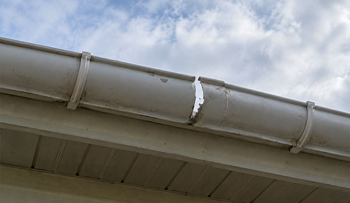 Cracked vinyl gutter showing structural damage along the roofline