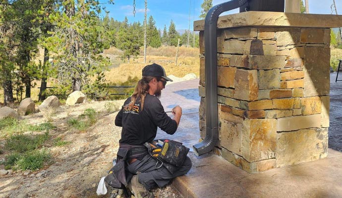 Technician installing a downspout directing water away from a stone foundation