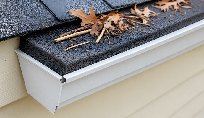 Porous foam gutter guard insert inside a gutter with dry leaves resting on top