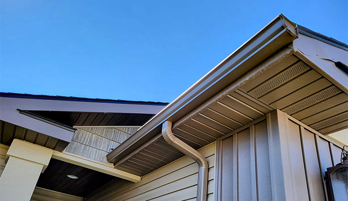 Bronze K-style gutter and downspout installed along the roofline of a modern residential home