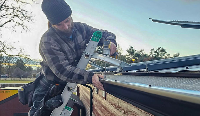 Technician on a ladder using a power drill to install a leaf guard screen over a residential rain gutter