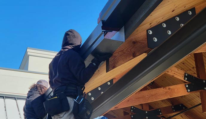 Workers installing gutters on a home roof structure with visible framing