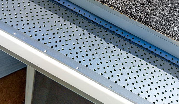Perforated metal aluminum gutter guard with hole patterns installed over a rain gutter