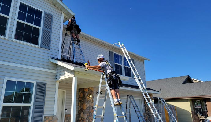 Professional installers working on gutters using ladders and safety equipment on a residential home
