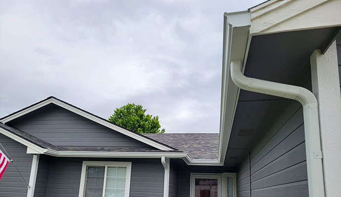 Gray residential home with white seamless K-style gutters and downspouts installed along multiple rooflines