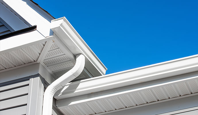 Clean white K-style gutter with downspout and end cap installed on a residential house under a clear blue sky