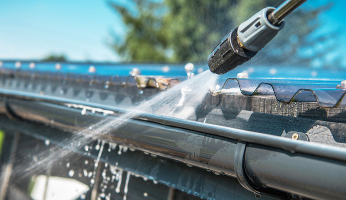 Pressure washer cleaning a roof gutter with water spray