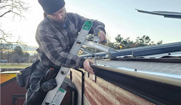 Technician installing new gutter sections along a residential roofline using a ladder and professional tools