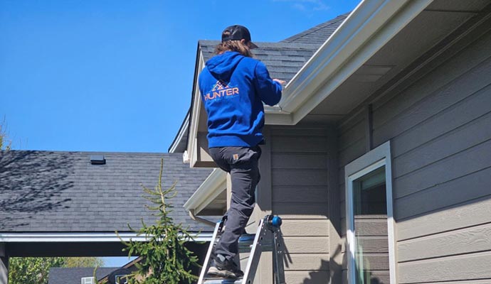 Gutter professional performing service on residential gutters using a ladder outside a home