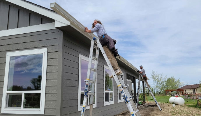 Workers installing gutters on a gray house using ladders
