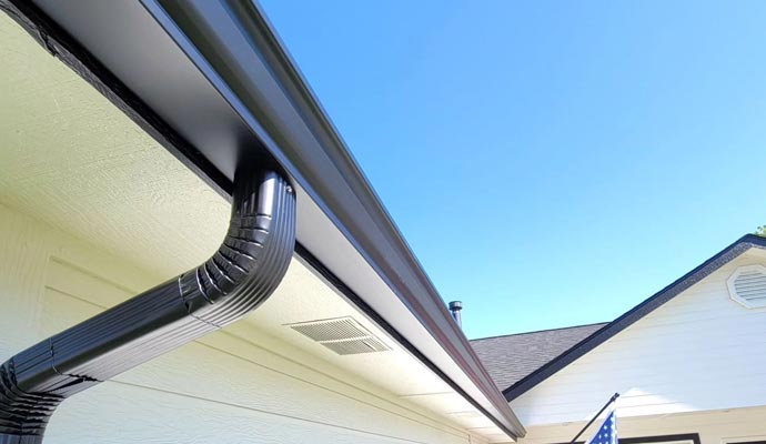 Modern rain gutter system with a curved metal downspout installed along the roof edge, designed to manage water flow efficiently and match the home’s exterior