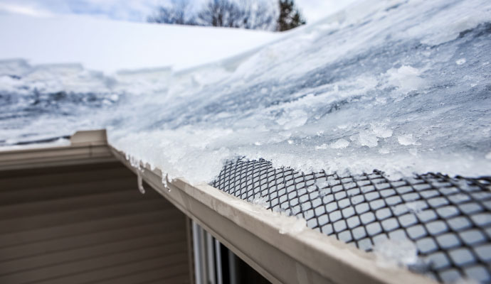 Snow-covered roof gutter guard along the edge of a house
